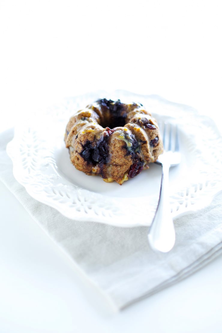 A head-on shot shows a mixed berry whole grain mini bundt cake on a small plate with a fork nearby.