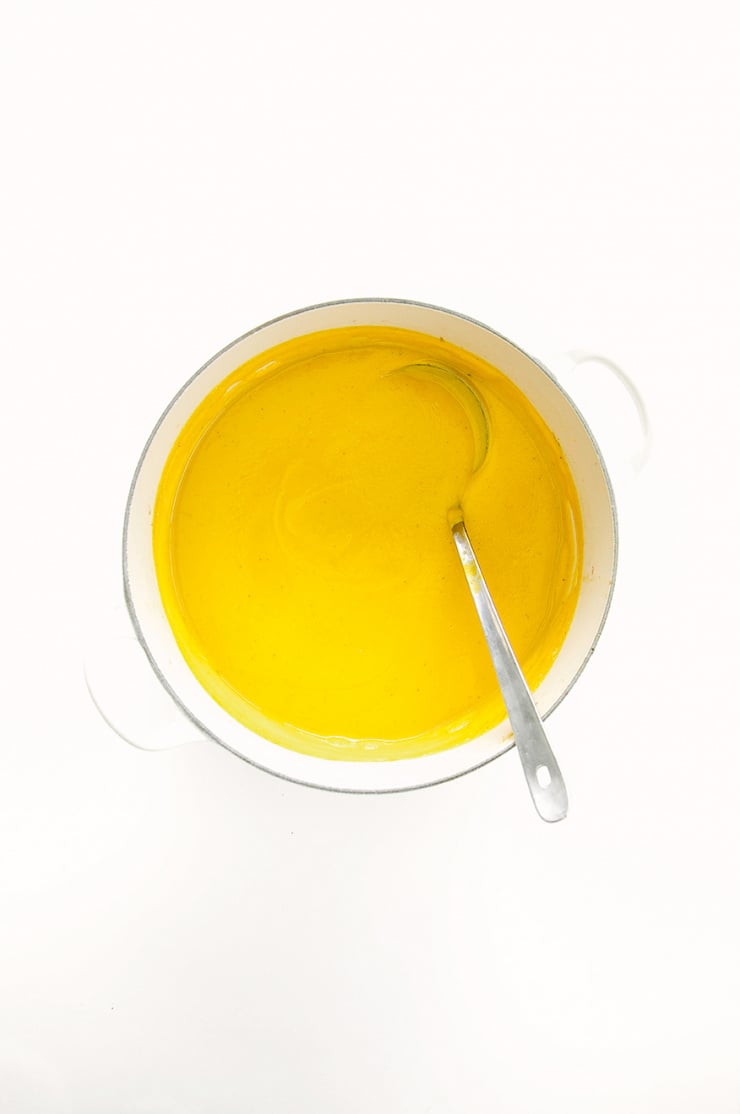 An overhead shot of a creamy pureed orange-hued soup in a pot.