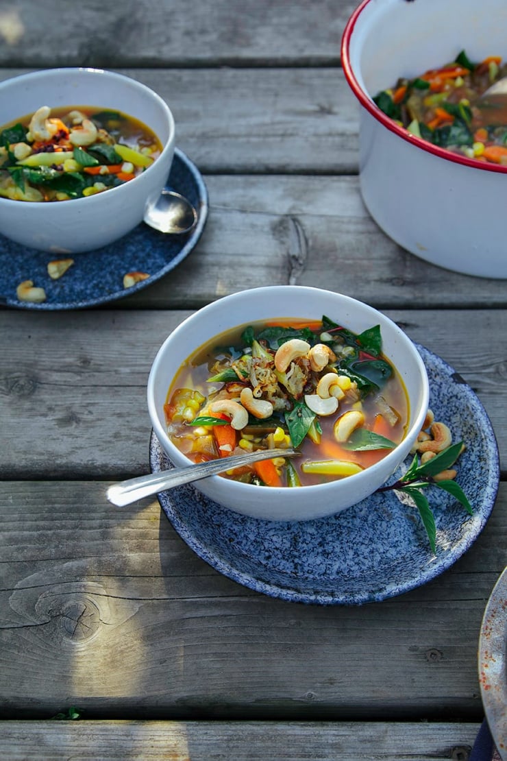 A 3/4 angle portrait shot of a bowl of garden vegetable stew topped with golden toasted cashews and crispy caramelized shallots.