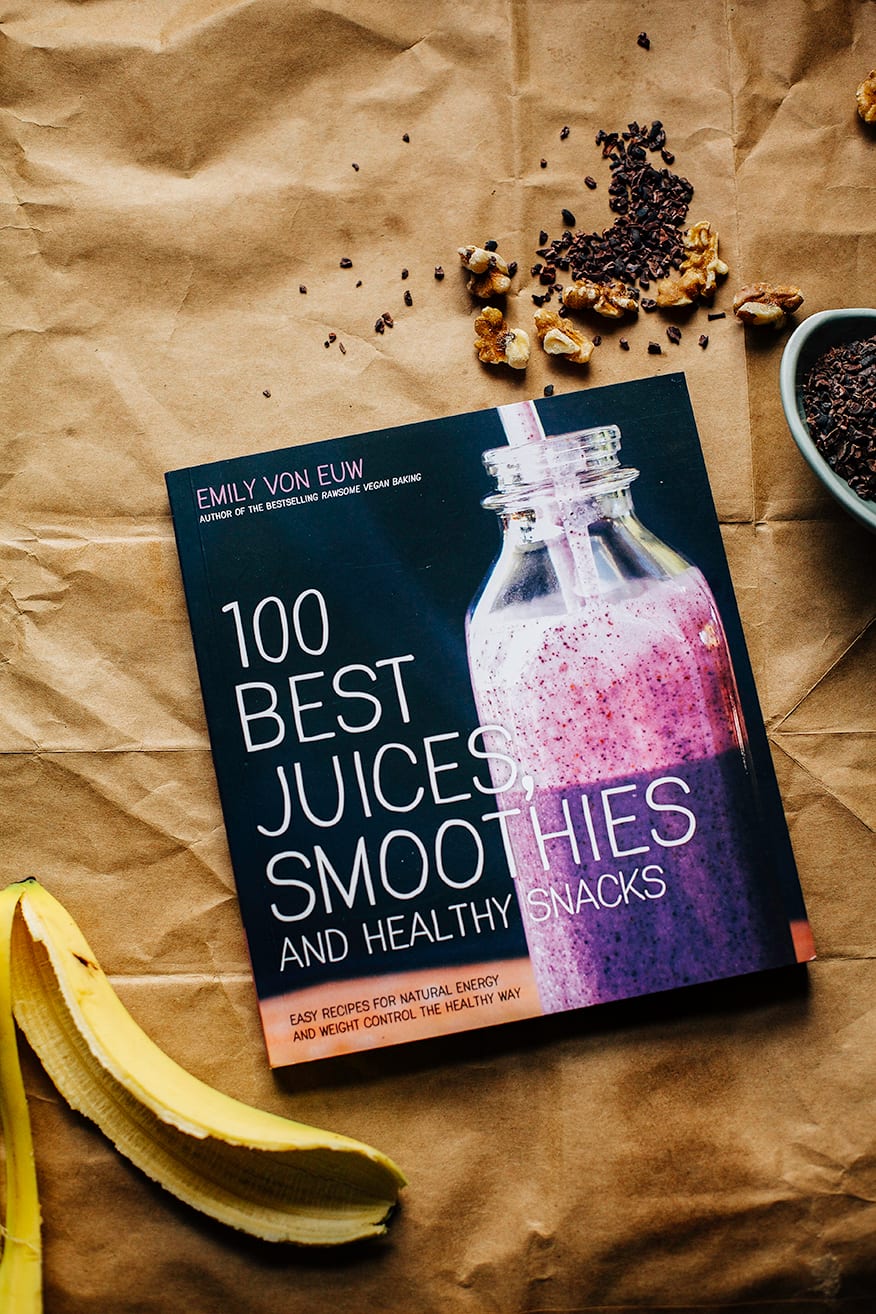 An overhead shot of Emily Von Euw's "100 Best Juices, Smoothies & Healthy Snacks" cookbook on a brown paper background.