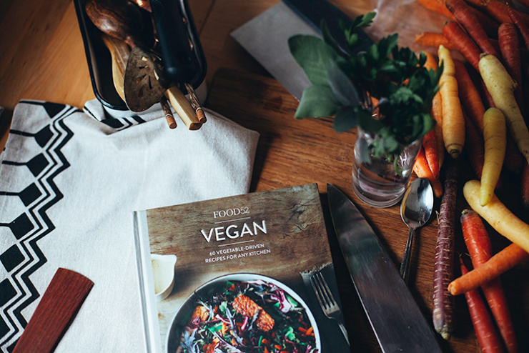 An overhead shot of the cookbook &ldquo;Food 52 Vegan&rdquo; surrounded by heirloom carrots, a chef&rsquo;s knife and some herbs.