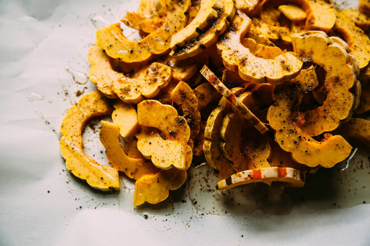 An overhead shot of cut delicata squash with spices sprinkled on top, pre-roasting.