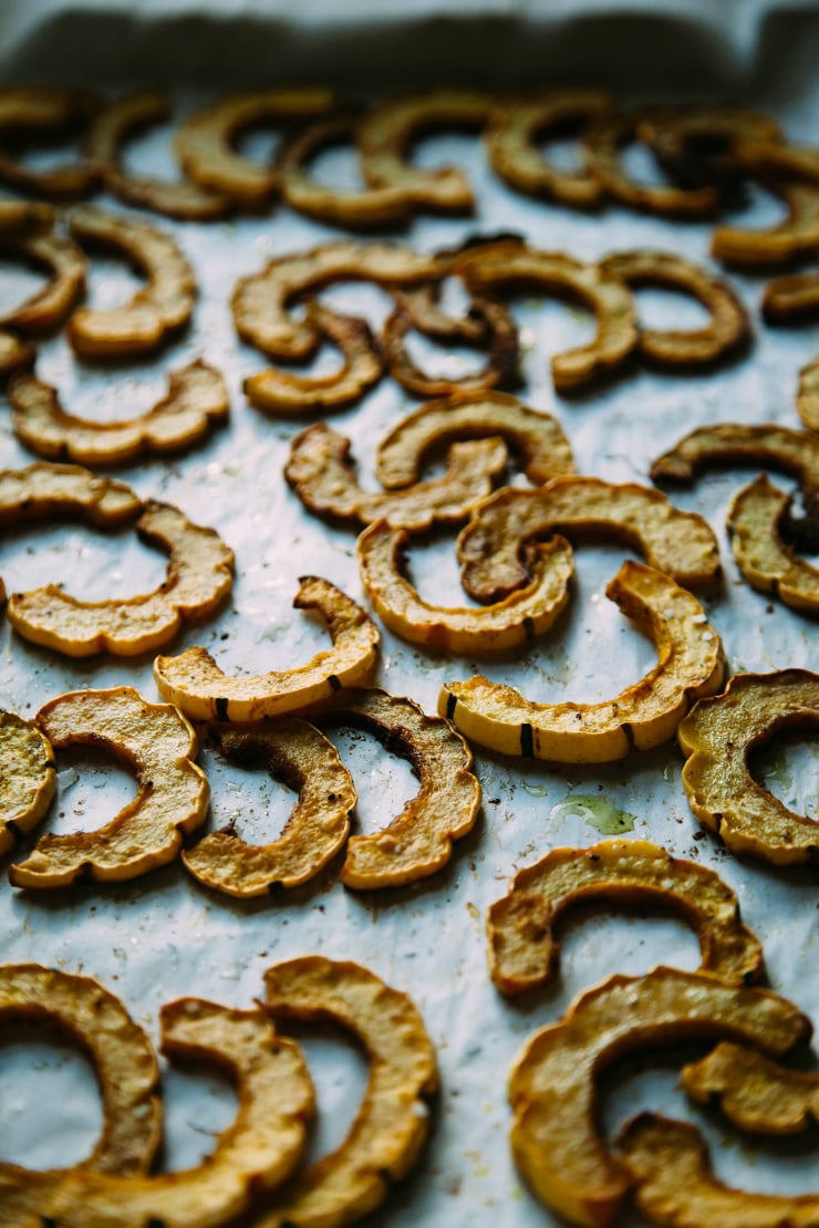 An up close image of roasted delicata squash half moons on a parchment lined baking sheet