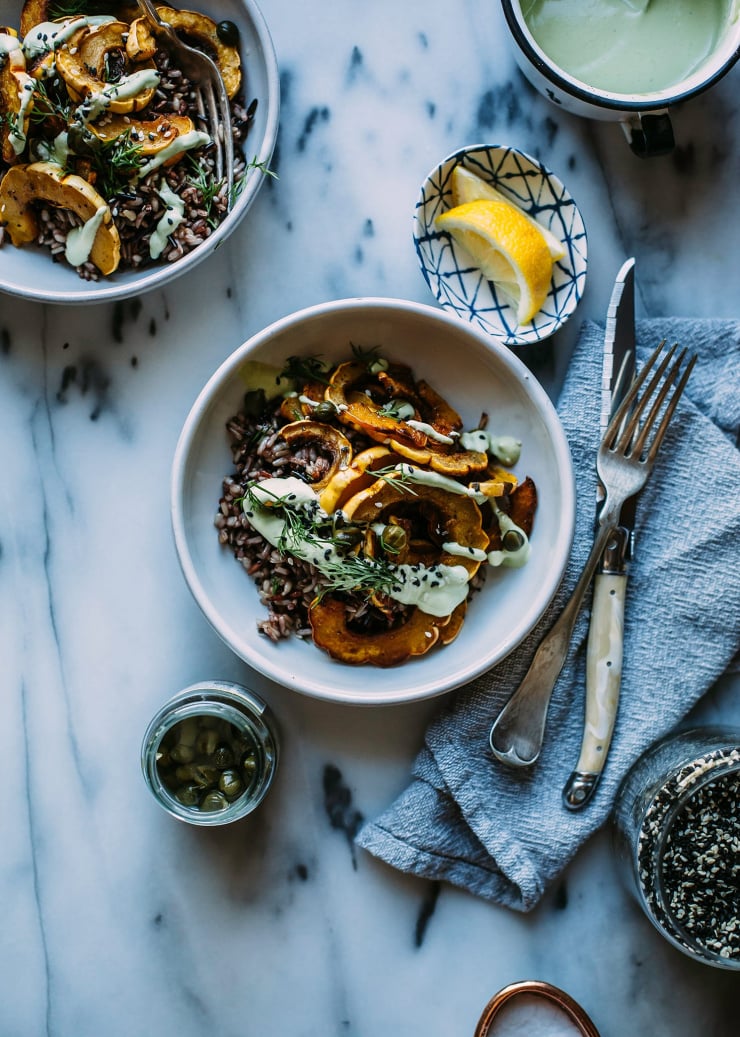 An overhead shot of a rice bowl with roasted pieces of squash and a drizzle of a creamy, light green sauce.