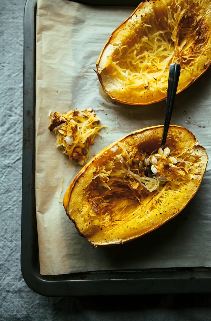An overhead shot of baked spaghetti squash halves on a parchment paper-lined baking sheet.