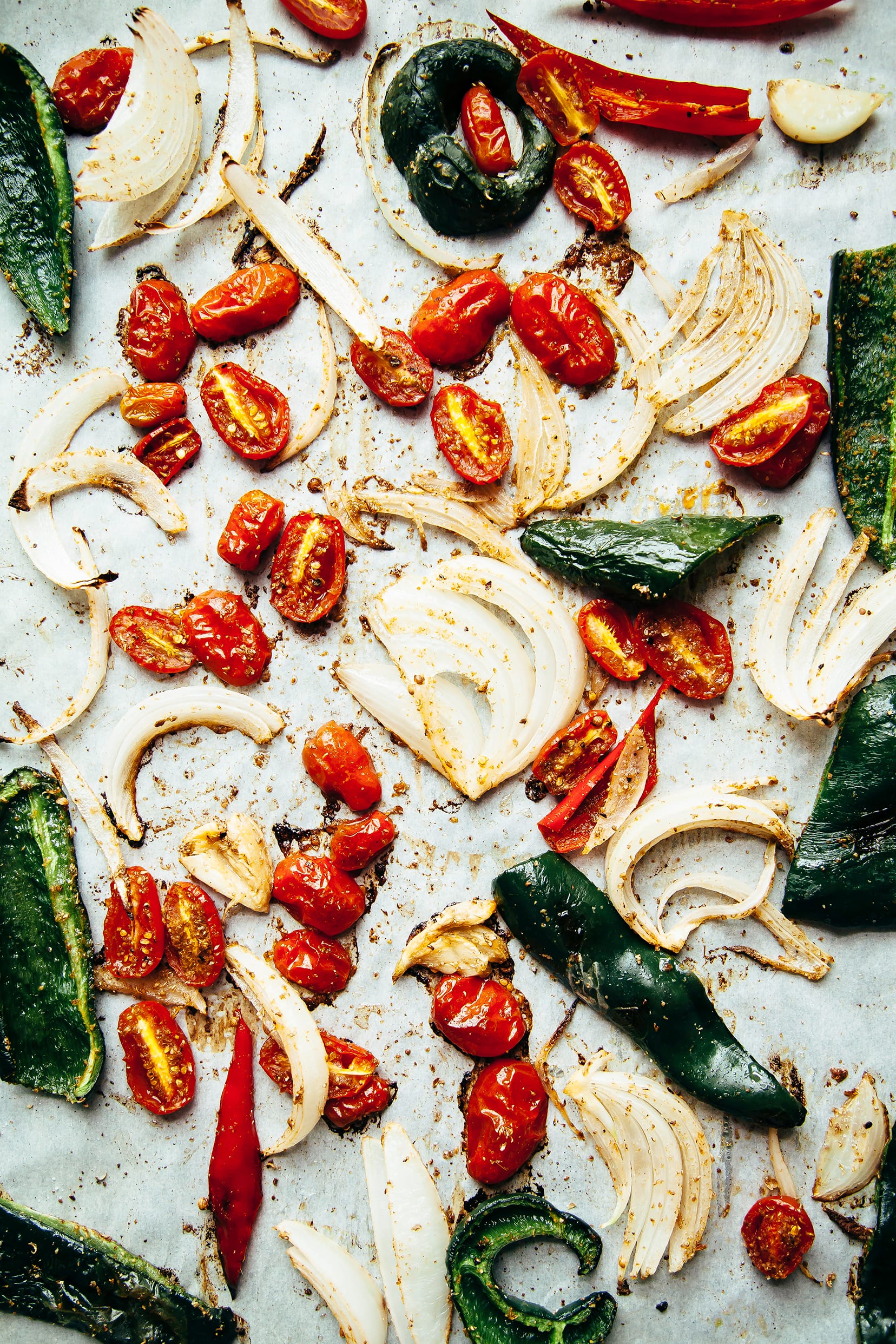 An up close, overhead shot of roasted onions, poblano peppers, and cherry tomatoes.