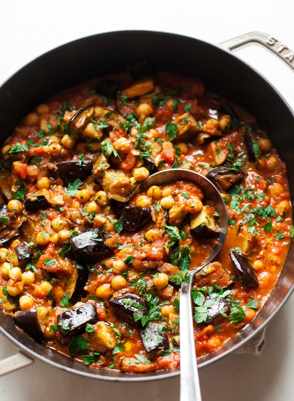 An overhead shot of a stew in a braiser-style pot, containing: seared chunks of eggplant, chickpeas, crushed tomatoes, spices, and chopped parsley.