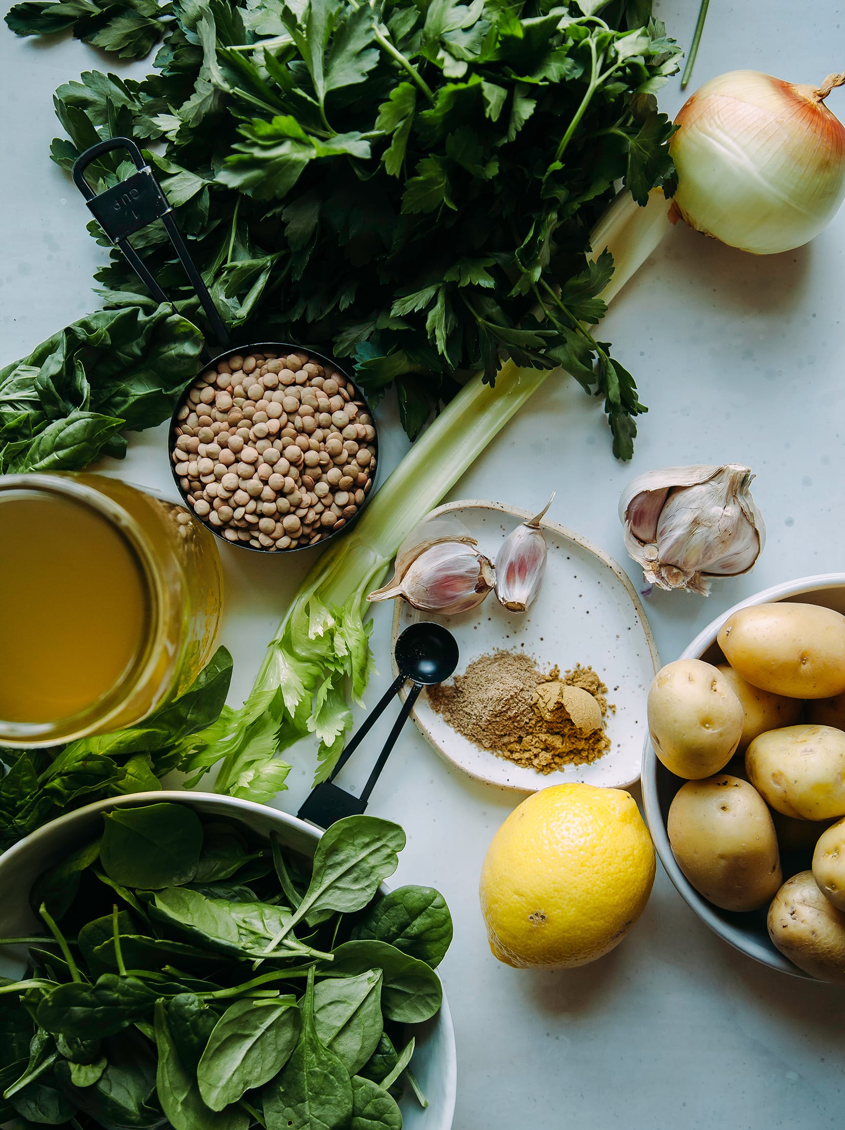 An overhead shot of ingredients for a deep green lentil stew with spinach and potatoes.