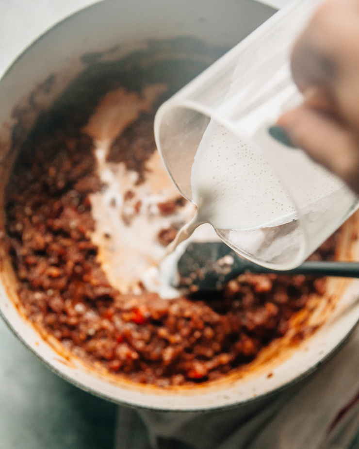 Image shows a bright white creamy liquid being added to a pot with a thick red sauce.