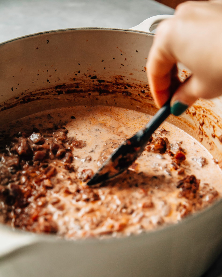 Image shows a hand holding a spatula stirring a vegan bolognese sauce.