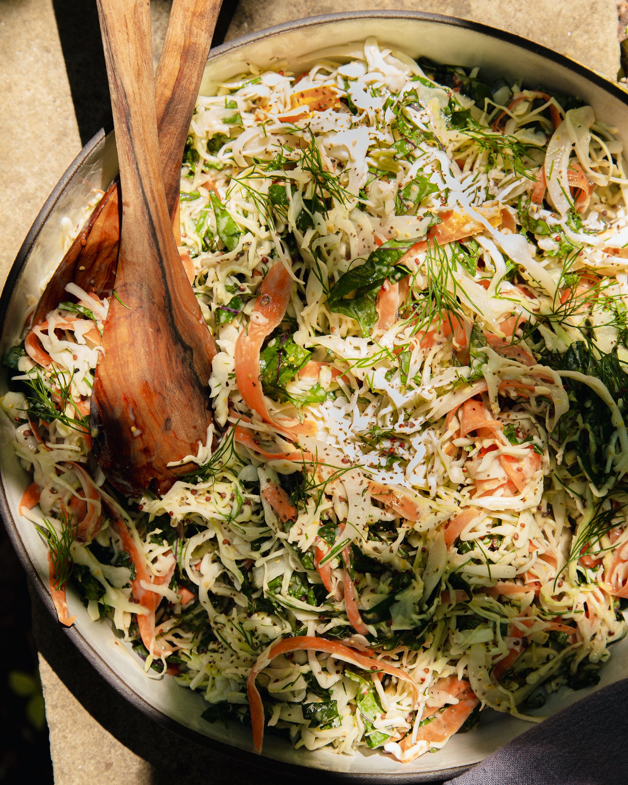 An up close, overhead shot of a cabbage, kale, and carrot slaw with creamy mustard dressing. The slaw is in a wide ceramic dish with a black rim.