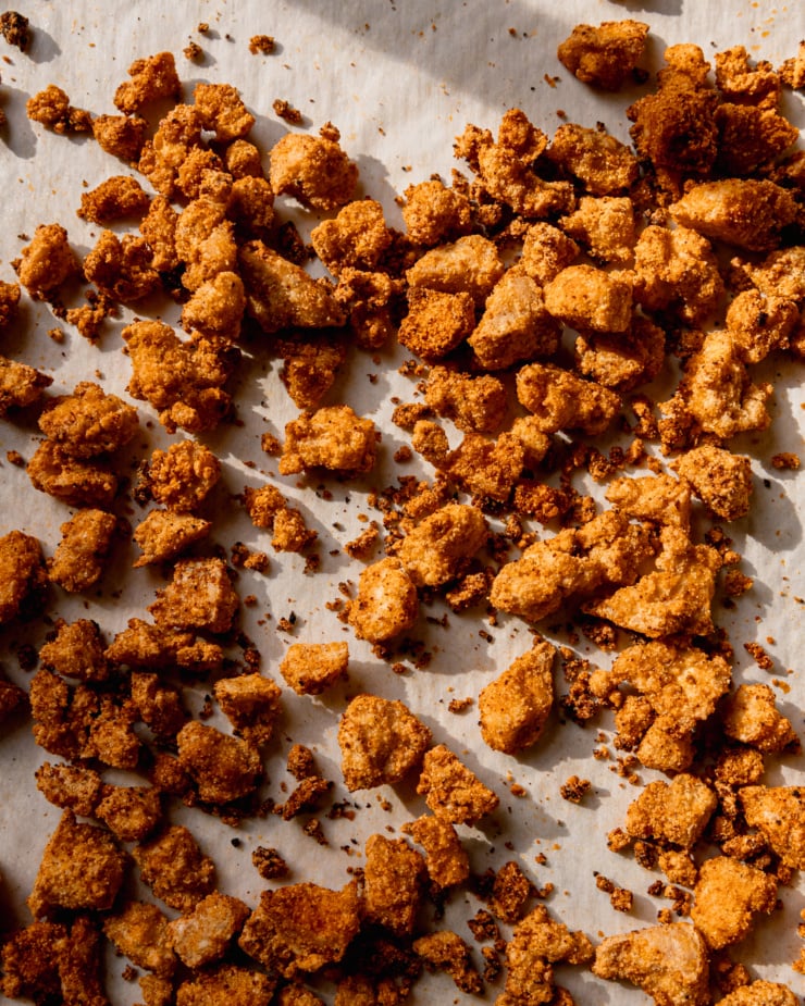 An overhead shot of crispy baked tofu bits against a white parchment background in harsh natural light.