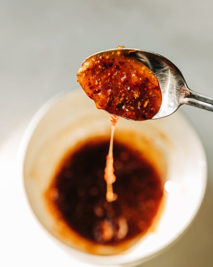 An up close shot shows a spoon dripping sticky apple cider reduction into a bowl below.