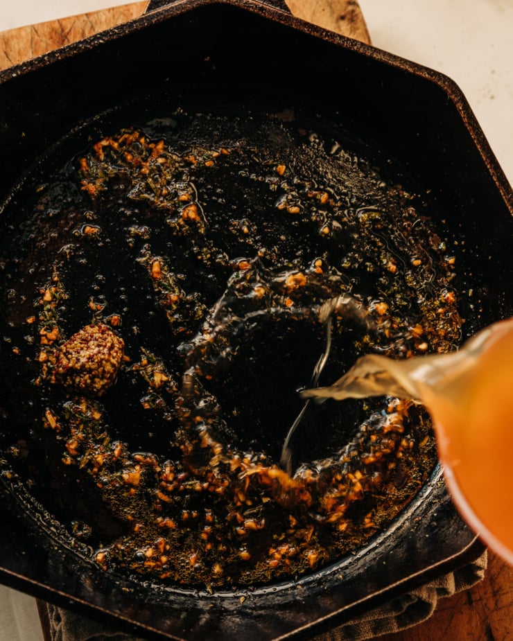 An overhead shot shows apple cider being poured into a skillet with garlic, minced rosemary, ground chillies, and grainy mustard.