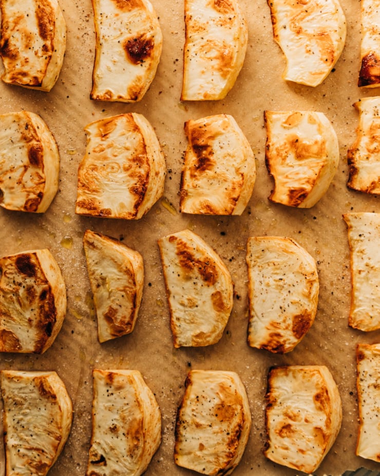 An overhead shot of caramelized, roasted wedges of celery root on a parchment lined baking sheet.