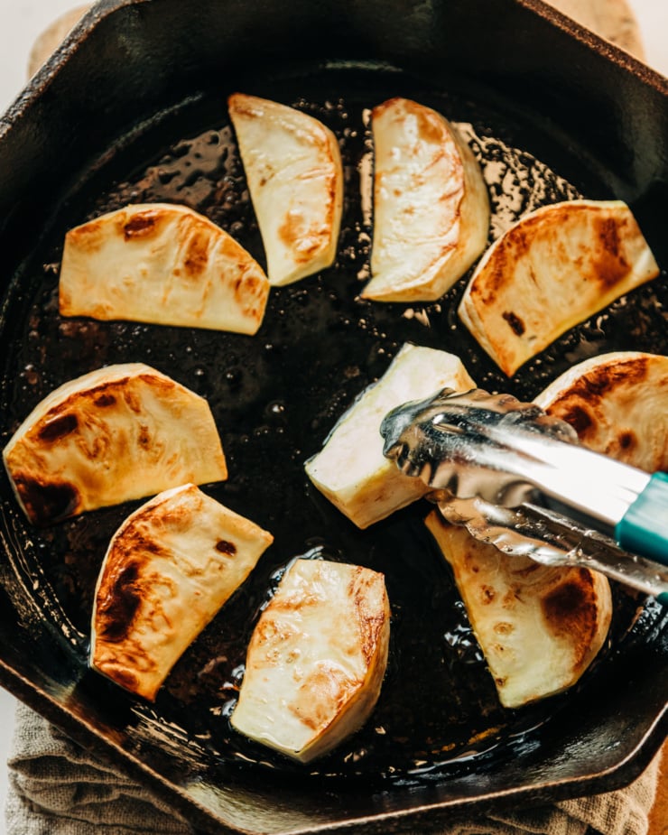 An overhead shot of celery root wedges getting seared in a skillet with hot oil.