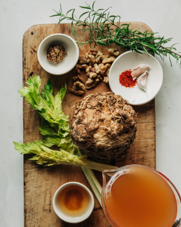 An overhead shot shows ingredients used in a cider glazed celery root side dish, all presented on a worn wooden cutting board.