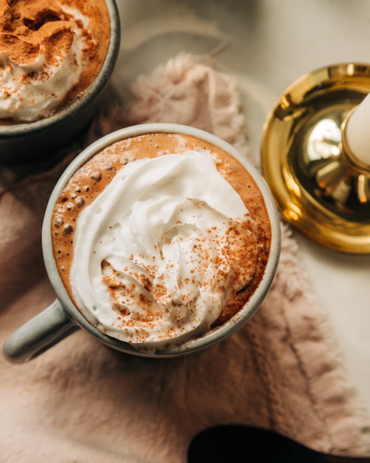 An overhead shot of vegan almond butter hot chocolate in a mug, topped with a swirl of coconut whipped cream and a sprinkle of cocoa powder.