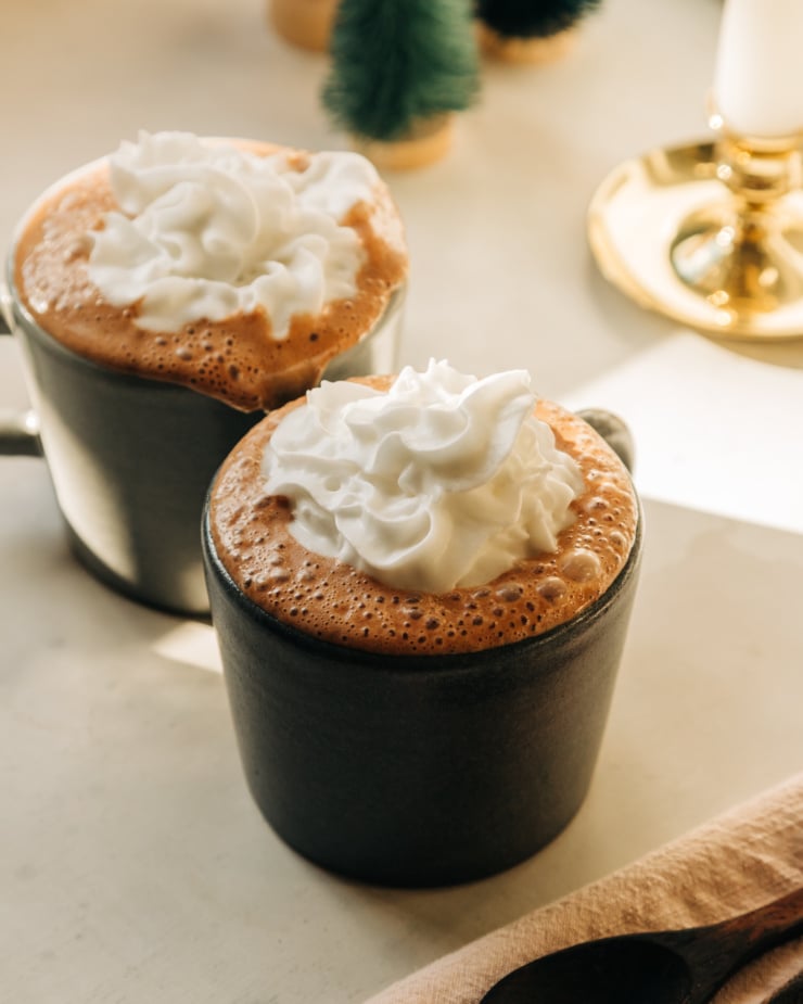 A head-on shot of two mugs of hot chocolate topped with lots of coconut whipped cream.