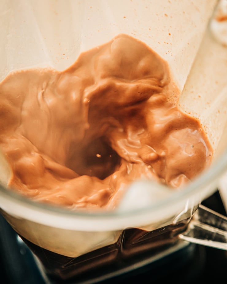 A 3/4 angle shot shows almond butter hot chocolate whipping up in a blender pitcher.