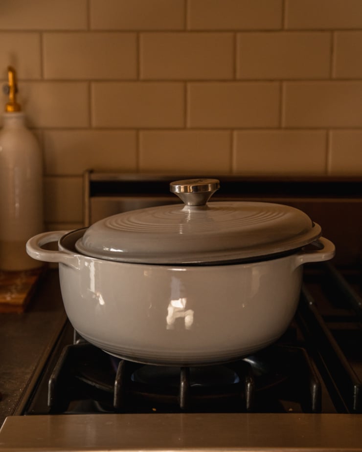 A head-on shot shows a grey Dutch oven on a gas stove with the lid slightly askew on top.