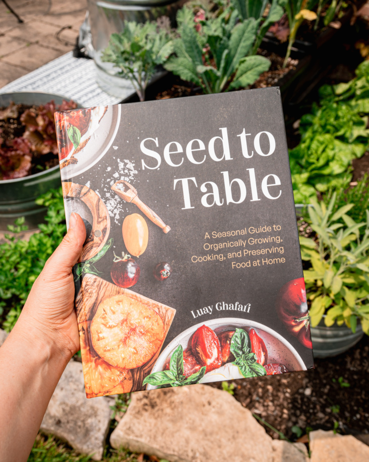An overhead shot shows a copy of Luay Ghafari's "Seed to Table" book being held by a hand against a patio vegetable garden backdrop.