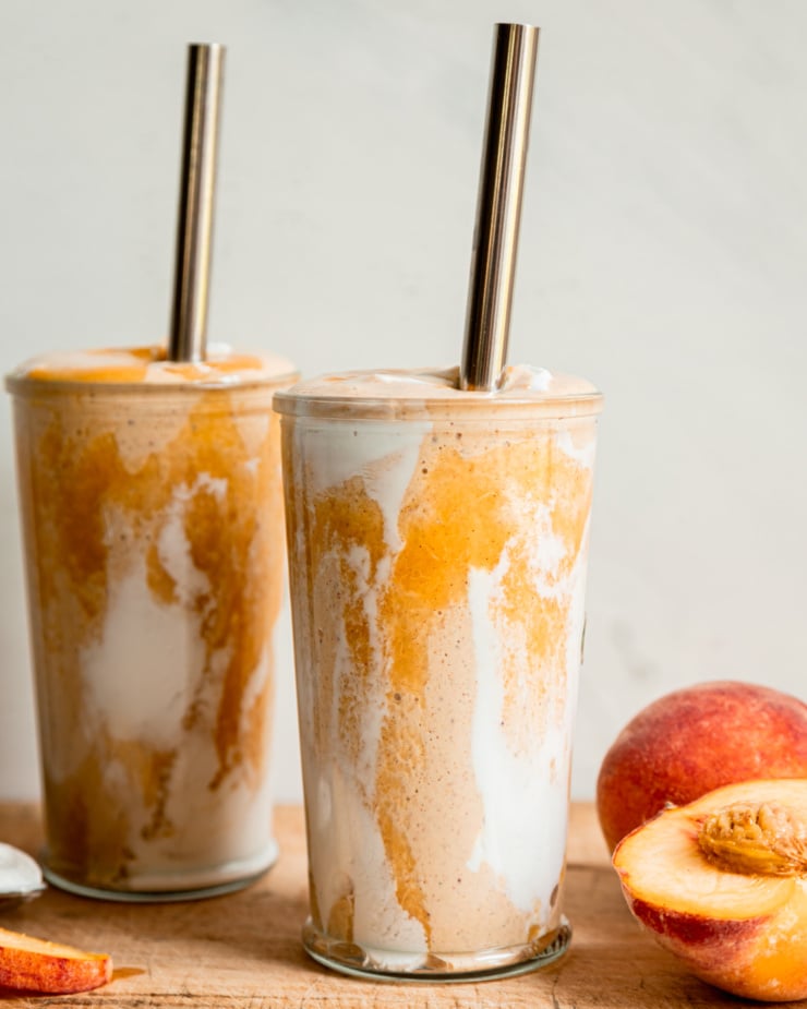 A head-on shot of a vegan peaches and cream protein smoothie in two glasses with metal straws. Peach purée and vegan yogurt create a tie dye effect on the glass.