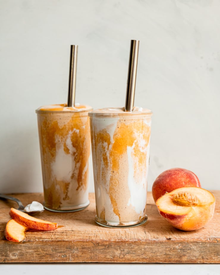 A head-on shot of a vegan peaches and cream protein smoothie in two glasses with metal straws. Peach purée and vegan yogurt create a tie dye effect on the glass.