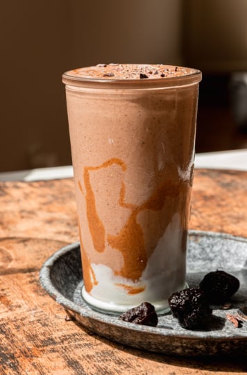 A head-on shot shows a glass of chocolate fiber smoothie with swirls of almond butter and vegan yogurt on the side of the glass.