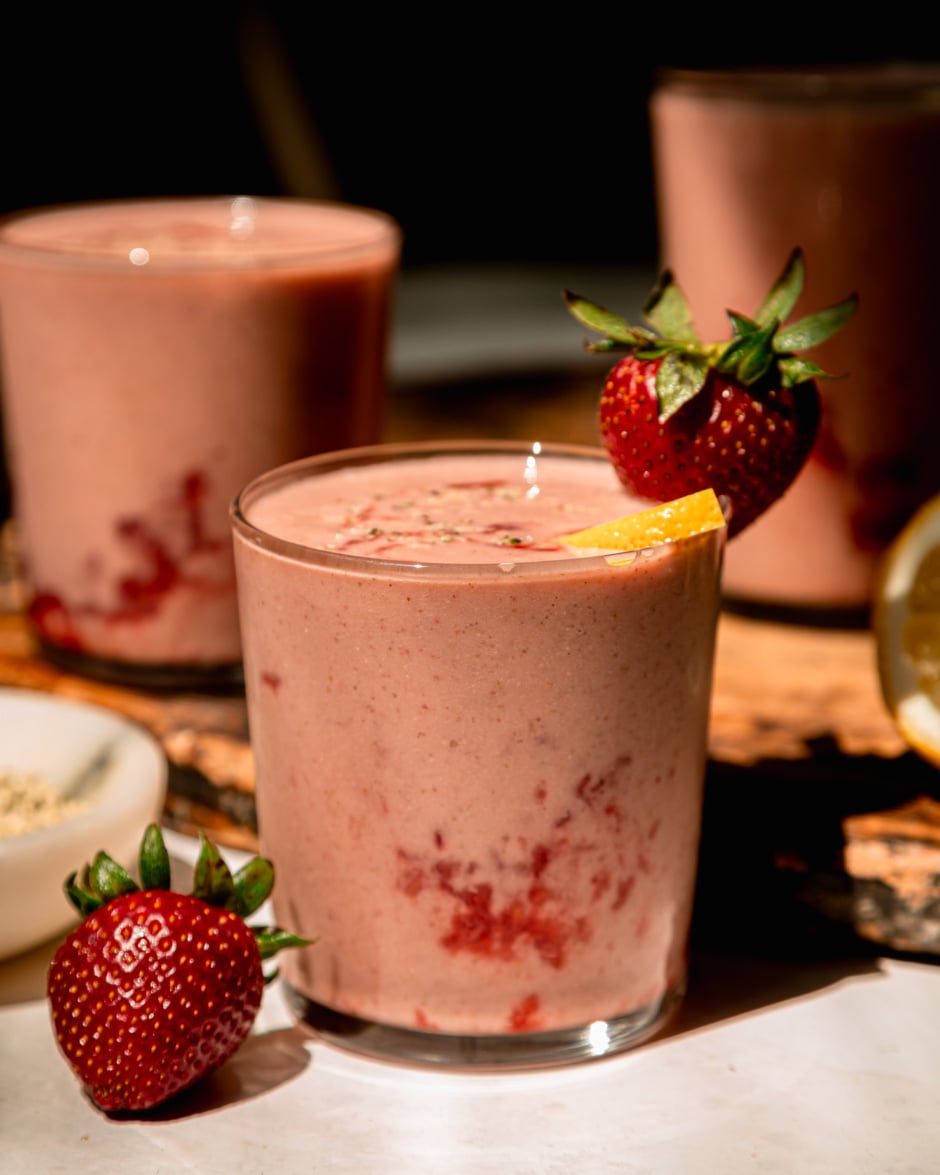 A head-on shot in direct sunlight shows a strawberry lemonade smoothie garnished with a whole strawberry and a little lemon slice.