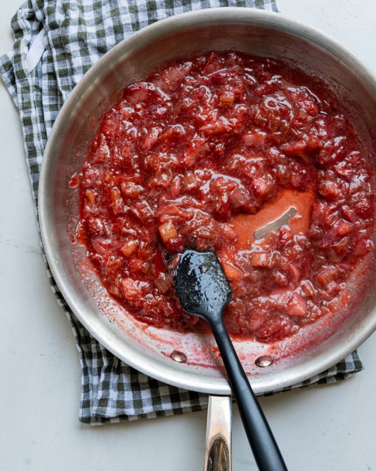 An overhead shot shows a rhubarb strawberry compote in a steel sauté pan with a spatula in the mix.