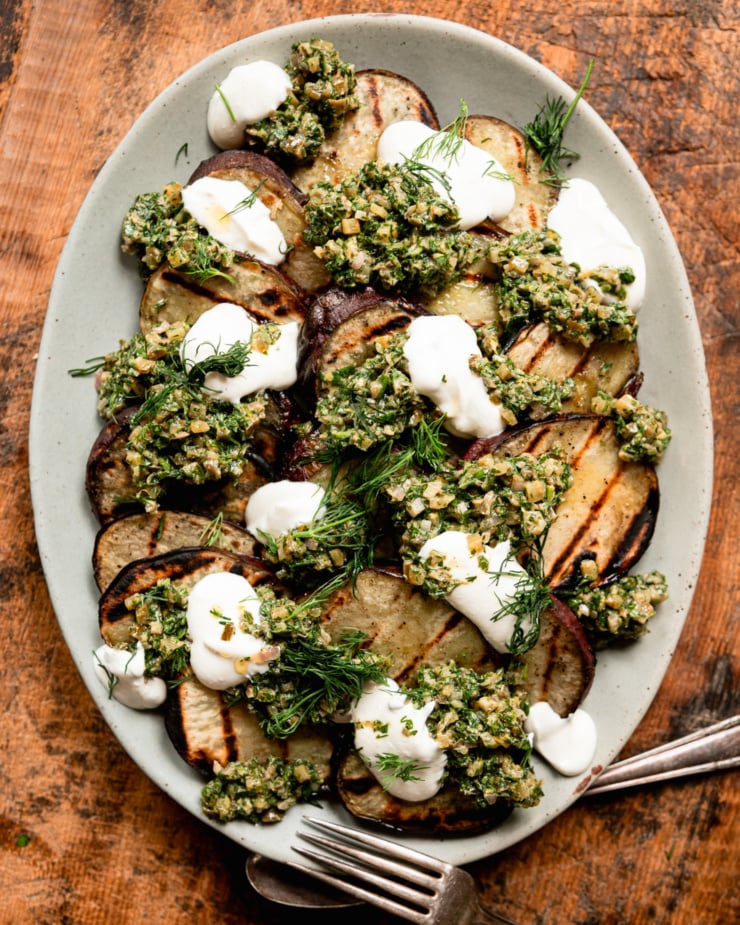 Overhead shot shows a pile of roasted Japanese sweet potato chips topped with dill pickles salsa verde, vegetarian sour cream and fresh dill.