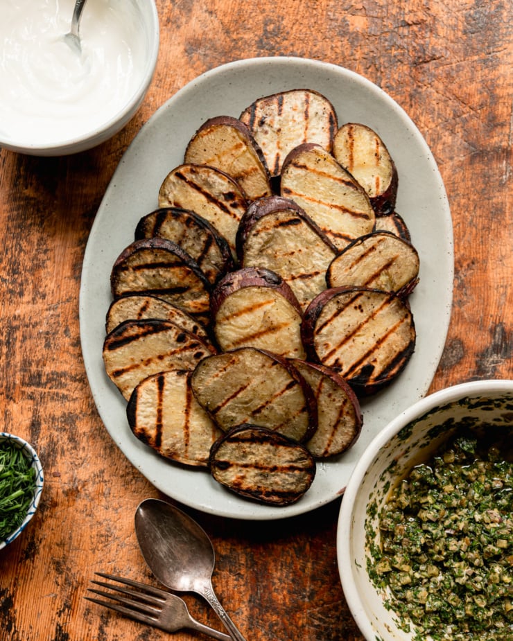 Overhead shot shows a pile of roasted Japanese sweet potato chips, a bowl of dill pickles salsa verde and a bowl of vegetarian sour cream.
