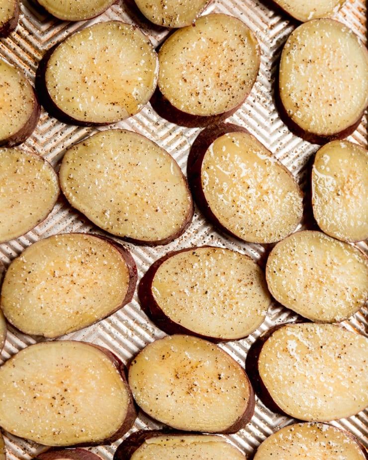 Overhead shot shows the potatoes thinly sliced, topped with olive oil and seasoned with salt and pepper.