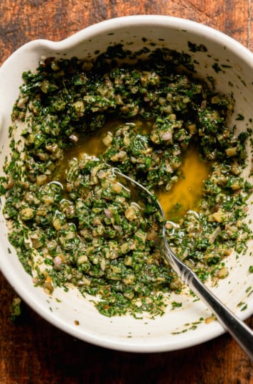 An overhead shot shows a bowl of dill pickle salsa verde with a spoon sticking out.