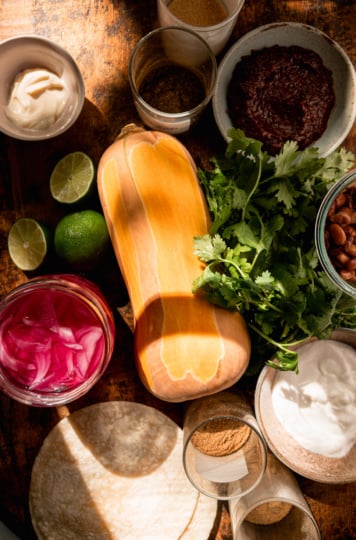 An overhead shot shows ingredients for vegan butternut squash tacos on a wood board.