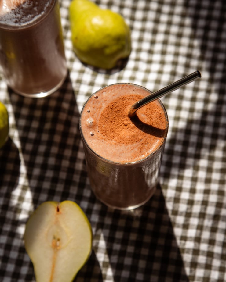 The overhead shot shows a cup of chocolate smoothie with the top of a napkin. The smoothie is decorated with cinnamon powder and a straw sticks out.
