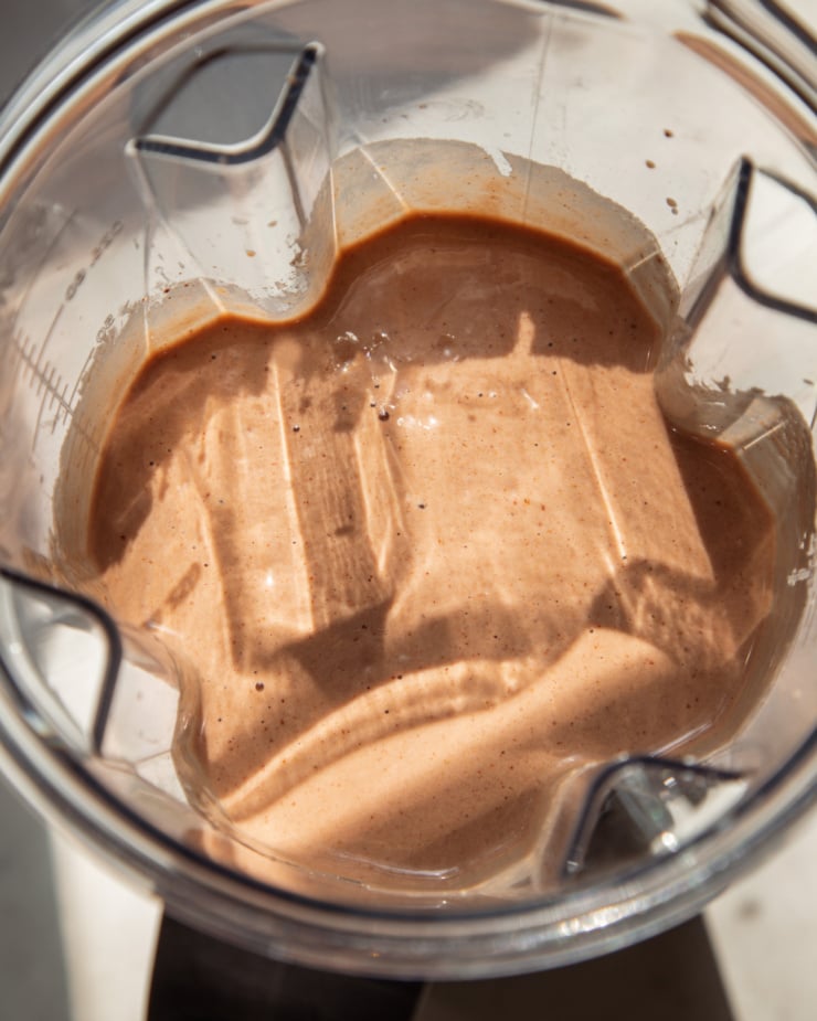 A close-up overhead shot shows a chocolate pear smoothie, freshly mixed in a Vitamix Blender jug in the sunny sun.