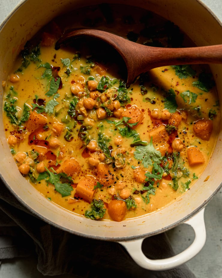 Overhead shot shows a pot of butternut squash stew. A wooden ladle sticks out of the pot. The broth looks creamy and golden.