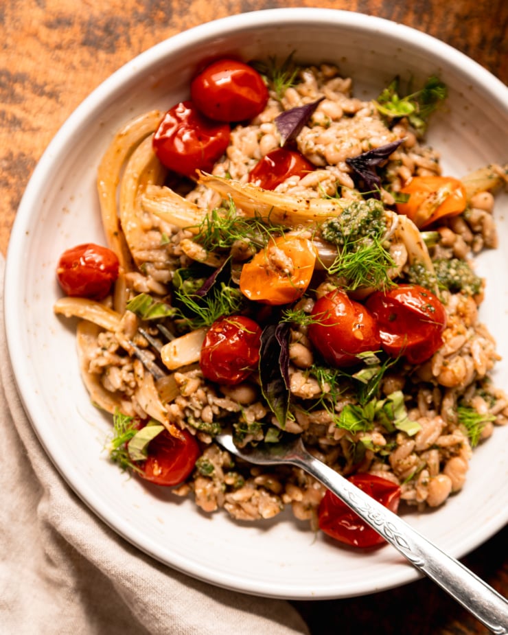 Overhead shot shows a wide bowl of pesto orzo. Sprinkle the Orzo and White Bean with roasted cherry tomatoes and fennel, as well as fresh basil and fennel leaves.