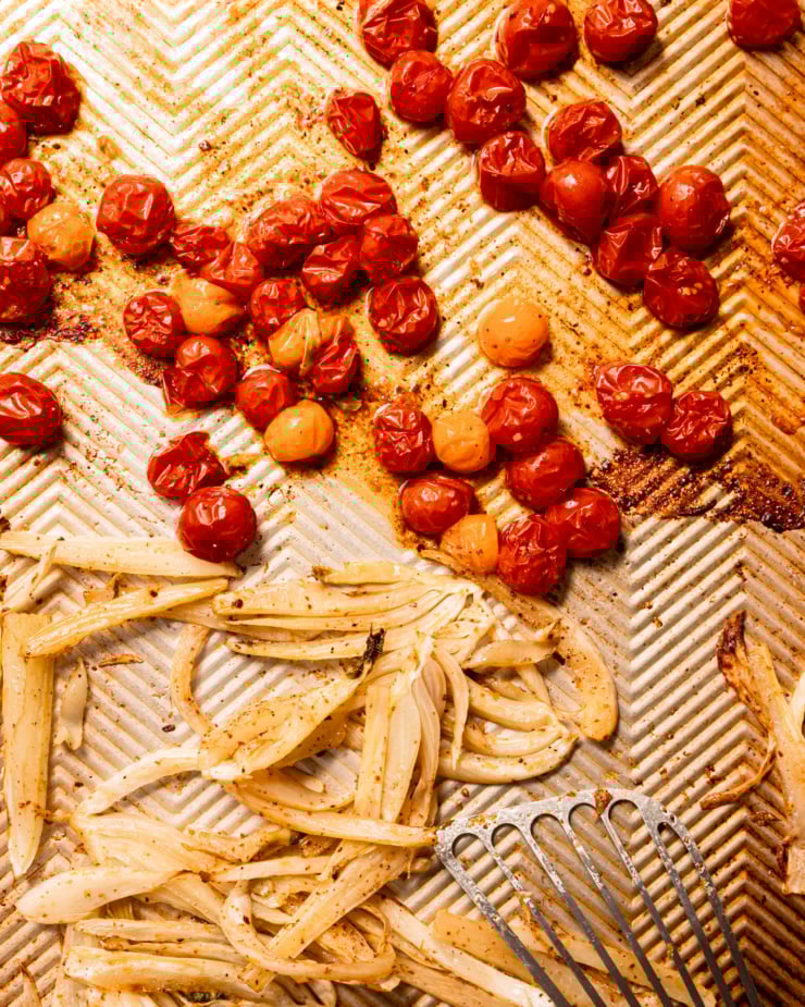 Overhead lens shows roasted cherry tomatoes and fennel on a baking tray.