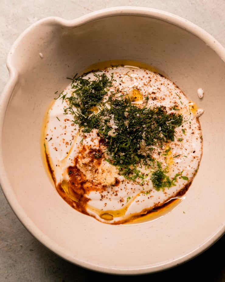 The overhead shot shows a bowl with yogurt with coconut milk, freshly chopped dill, tamari, olive oil, lime crust, salt, pepper and fine large garlic.