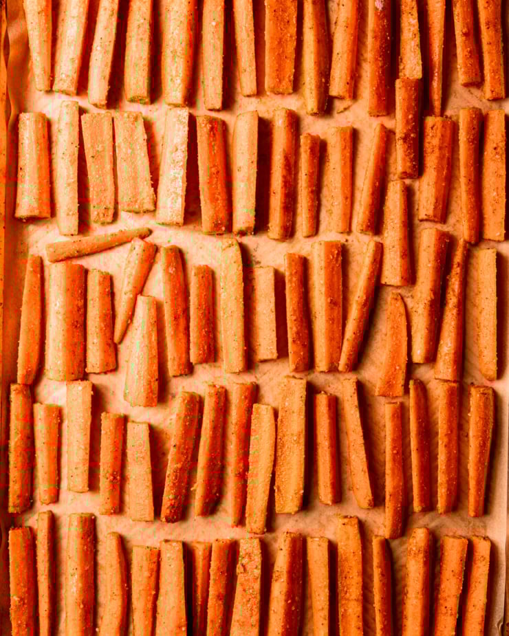 Overhead shot shows carrot sticks arranged in perfect rows on a parchment-lined baking tray.