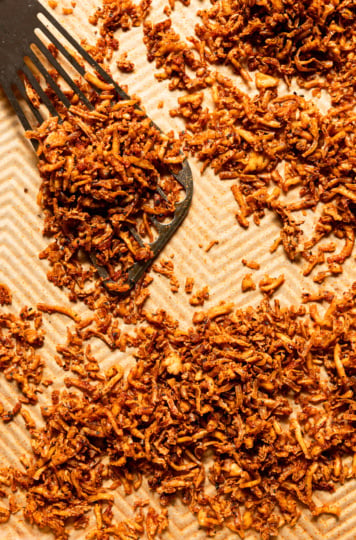 An overhead, up close shot shows a baking sheet filled with crispy and chewy baked shredded tofu. A metal spatula is seen to the side.