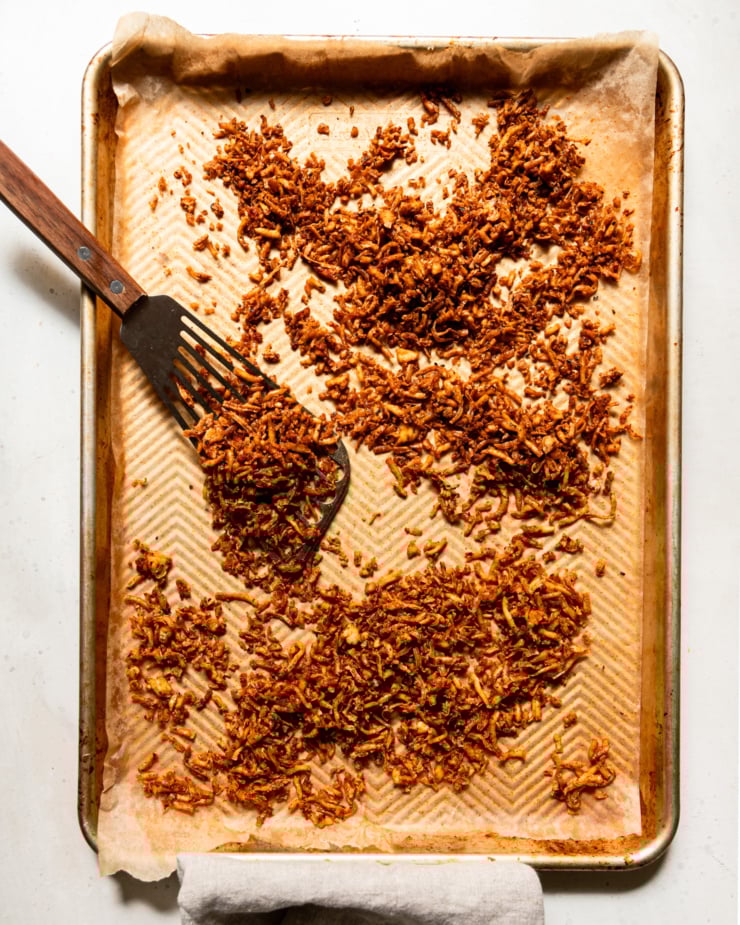 The top-down photo shows a baking sheet filled with crispy and chewy shredded grilled tofu. A metal spatula can be seen nearby.