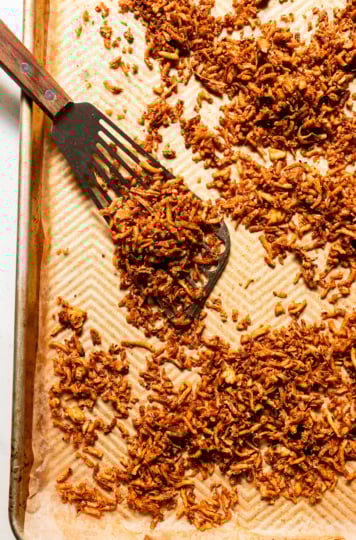 An overhead shot shows a baking sheet filled with crispy and chewy baked shredded tofu. A metal spatula is seen to the side.