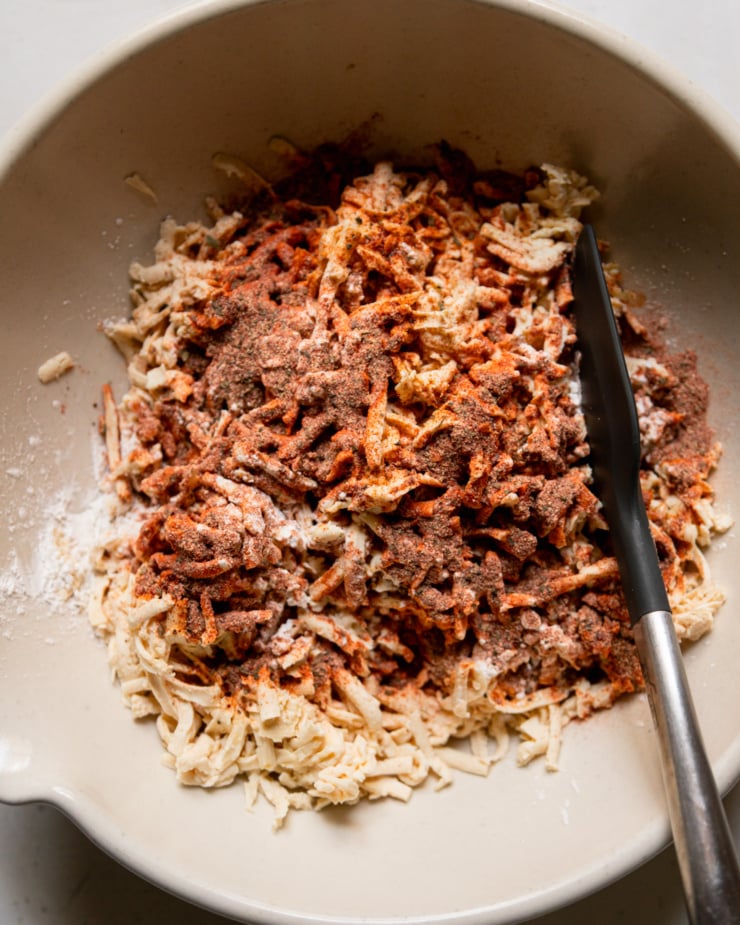 An overhead view shows a bowl of shredded tofu and a spatula. The tofu is sprinkled with cornstarch and spices.