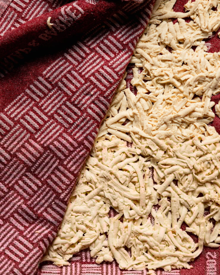A close-up overhead shot shows shredded tofu that has just been pressed dry with a towel and blotted dry.