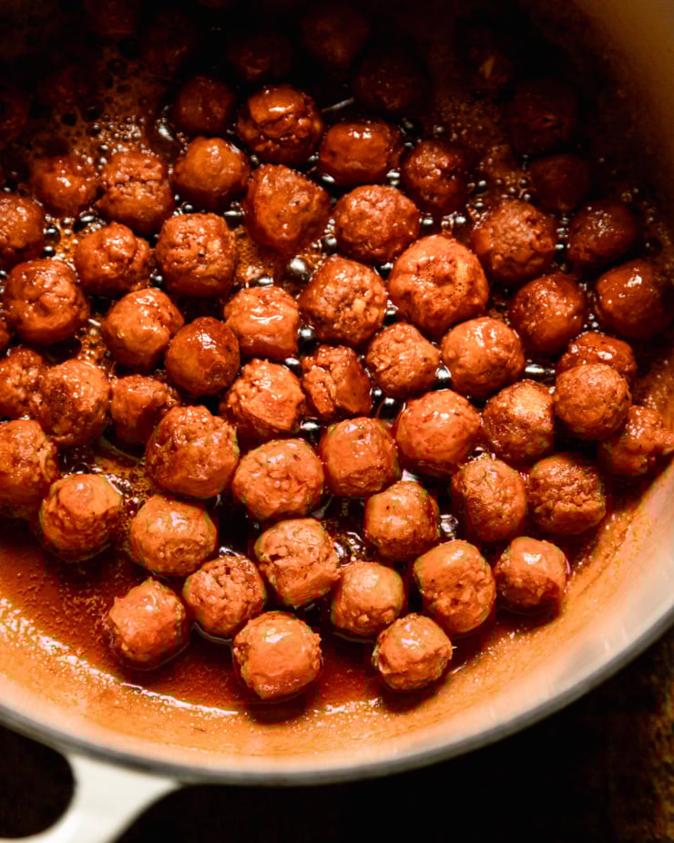 A close overhead shot shows small vegan sausage meatballs in a Dutch oven. They sparkle.