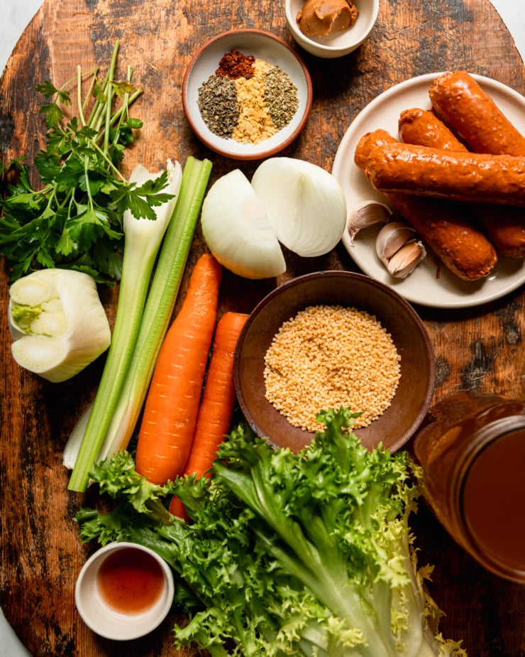 An overhead shot shows the ingredients for a vegetarian Italian wedding soup recipe; all on a rough wooden board.